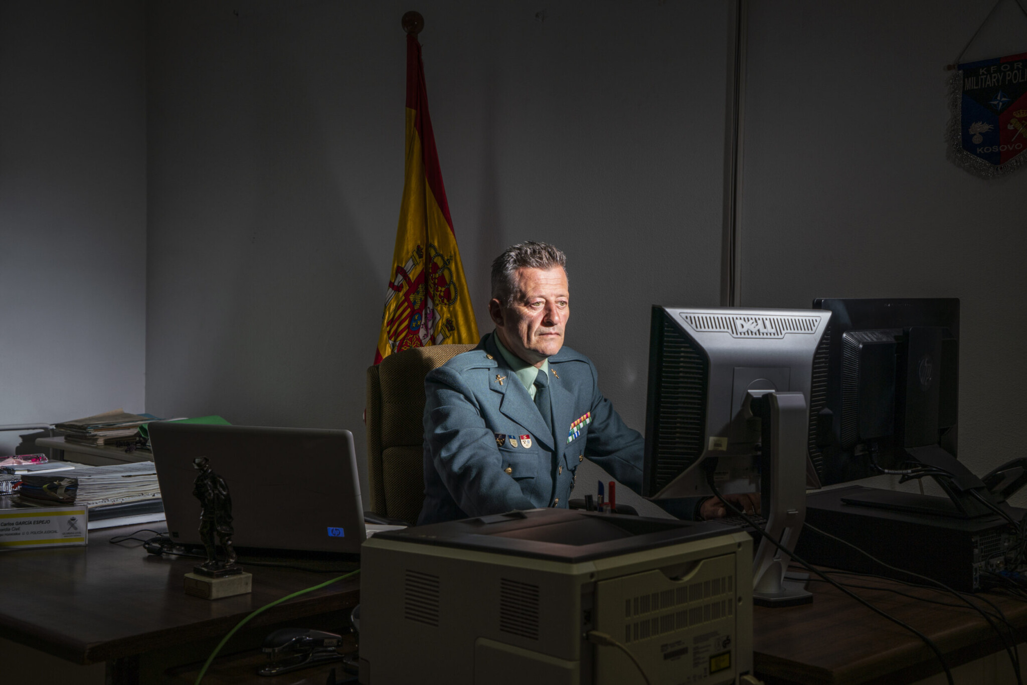 Mann in Uniform arbeitet am Schreibtisch, konzentrierter Blick auf Monitor, offizielles Umfeld
